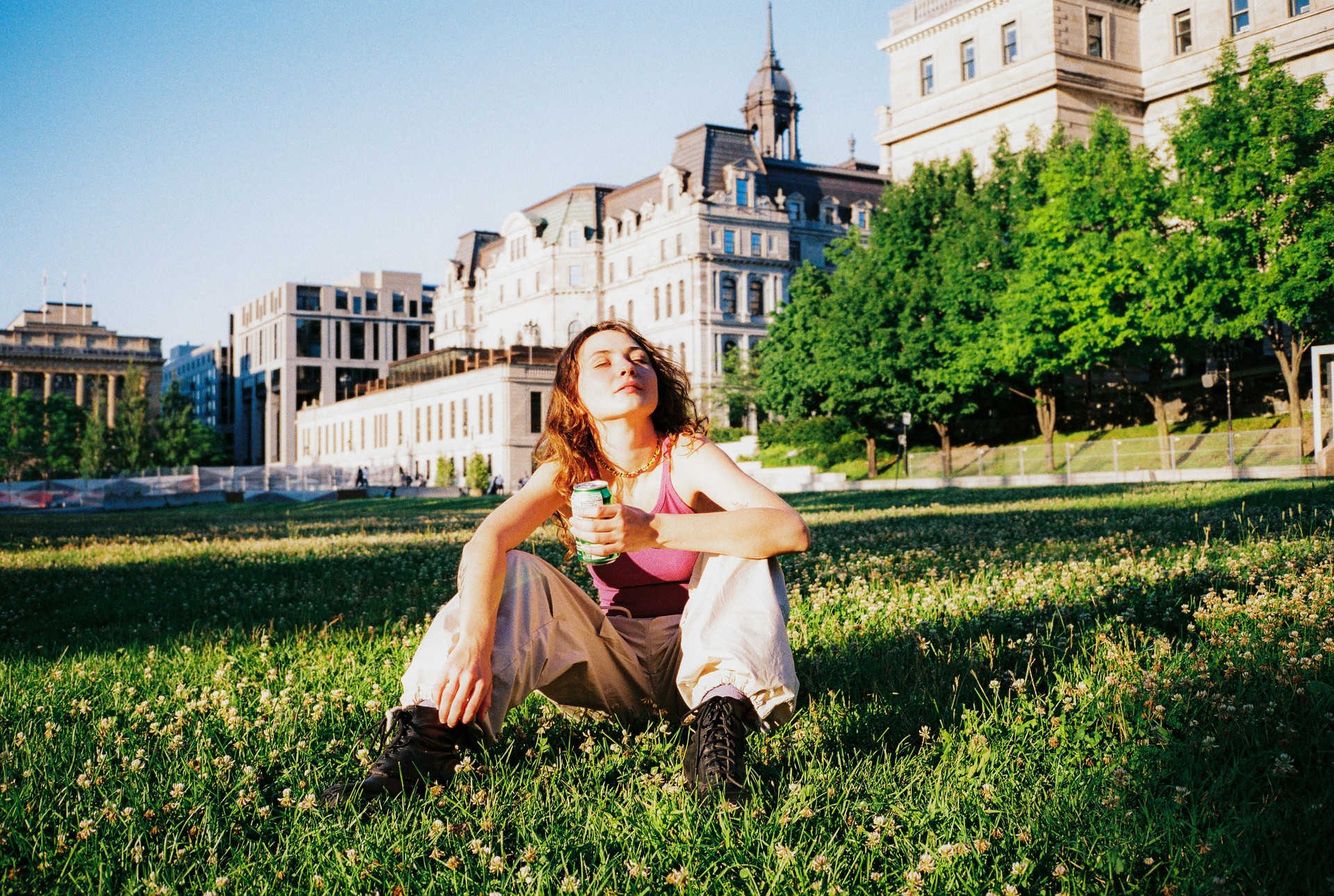 Woman with drink can sitting on the lawn in Montreal enjoying sunshine